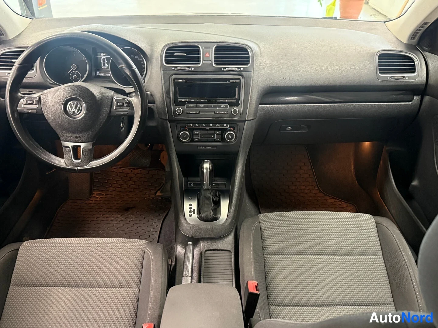 Edestä: Volkswagen Golfin kojelauta ja etumatkustustila ylhäältä kuvattuna: ohjauspyörä, keskikonsoli, automaattivaihteiston valitsin ja tummat etuistuimet.