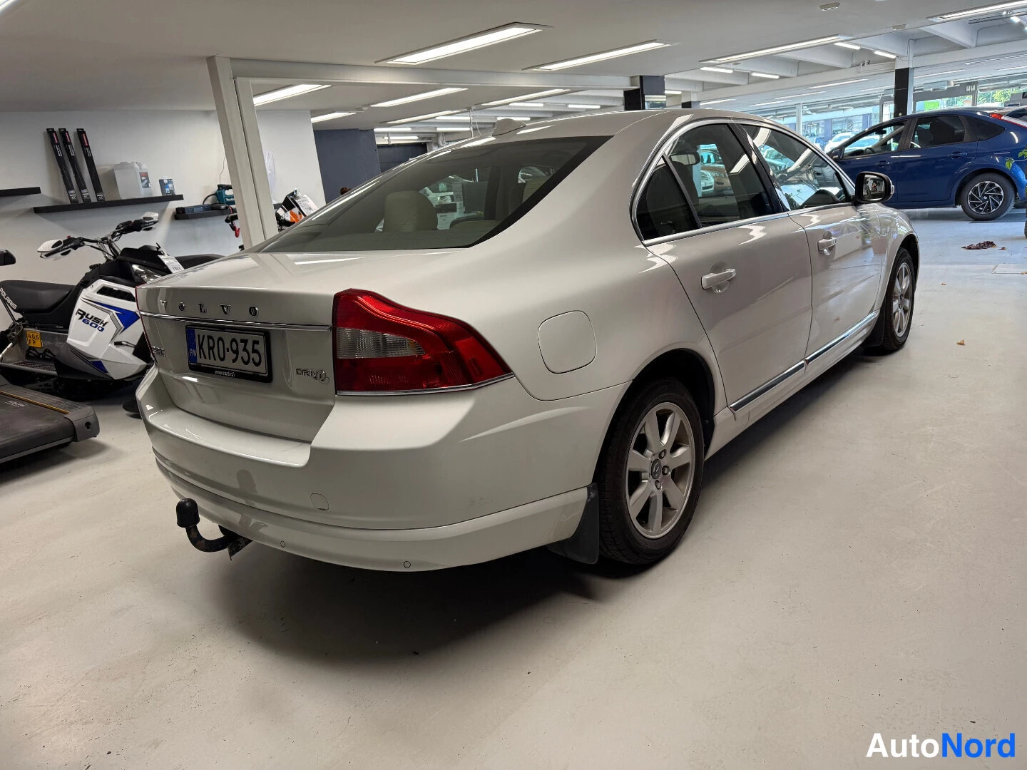 Takaviisto: Valkoisen sedanin perä ja oikea kylki; rekisterikilpi, vetokoukku ja DRIVe-merkintä tavaratilan kannessa.