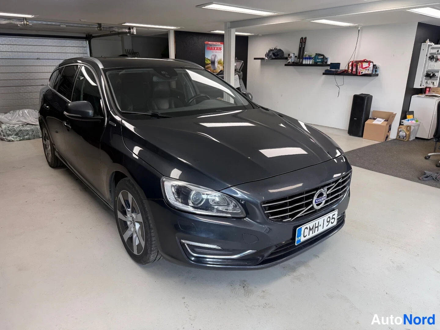 Etuviisto, nokka oikealle: Tummansininen Volvo V60 -asema-auto kolmesta neljäsosasta edestä oikealta kuvattuna autotallissa; rekisterikilpi CMH-I 95.