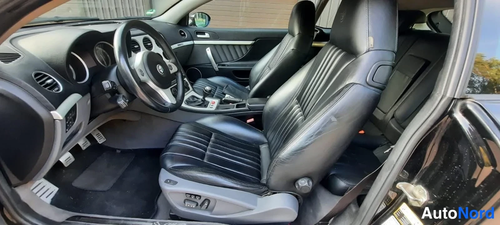 Muu: Auton sisätilat: mustat nahkaistuimet, Alfa Romeo -ohjauspyörä ja harmaa keskikonsoli.