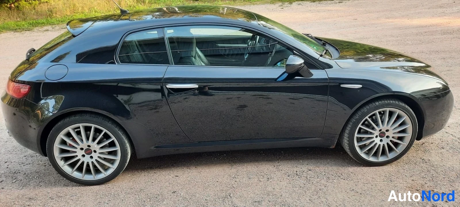 Takaviisto: Mustan Alfa Romeo Breran takakolmasosan sivunäkymä hiekkateellä.