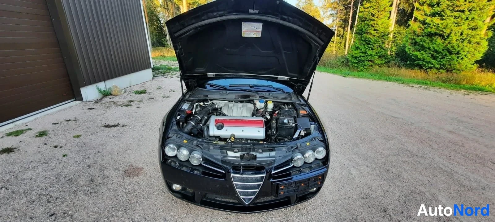 Edestä: Mustan auton avoin moottoritila etunäkymässä, punainen moottorikansi näkyvissä.