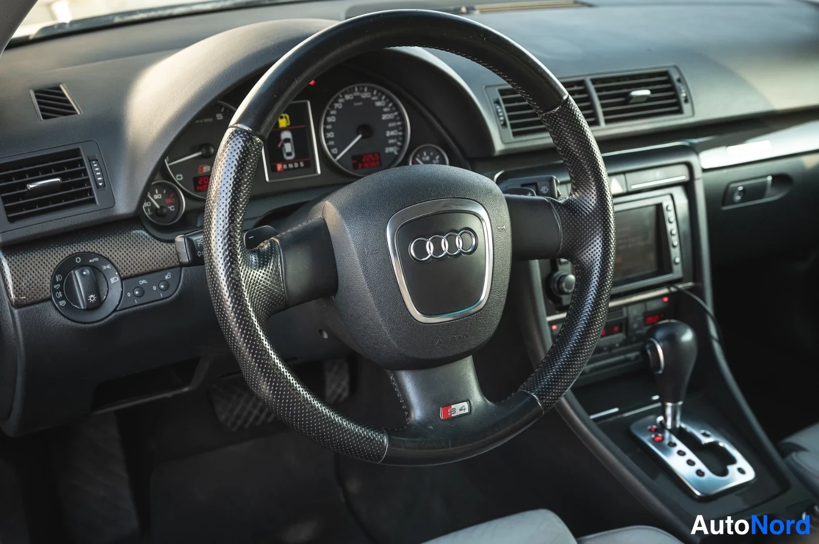 Muu: Ohjauspyörä Audi-merkillä ja S4-merkillä, taustalla mittaristo, keskikonsolin näyttö ja automaattivaihteen valitsin.