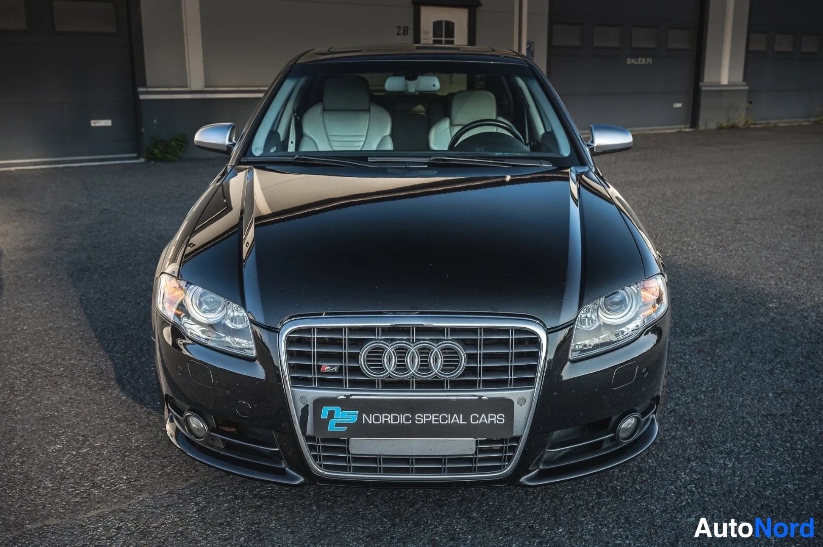 Edestä: Suora etukuva mustasta Audi S4 -sedanista: etusäleikkö Audi-logoineen, ajovalot ja Nordic Special Cars -kyltti.