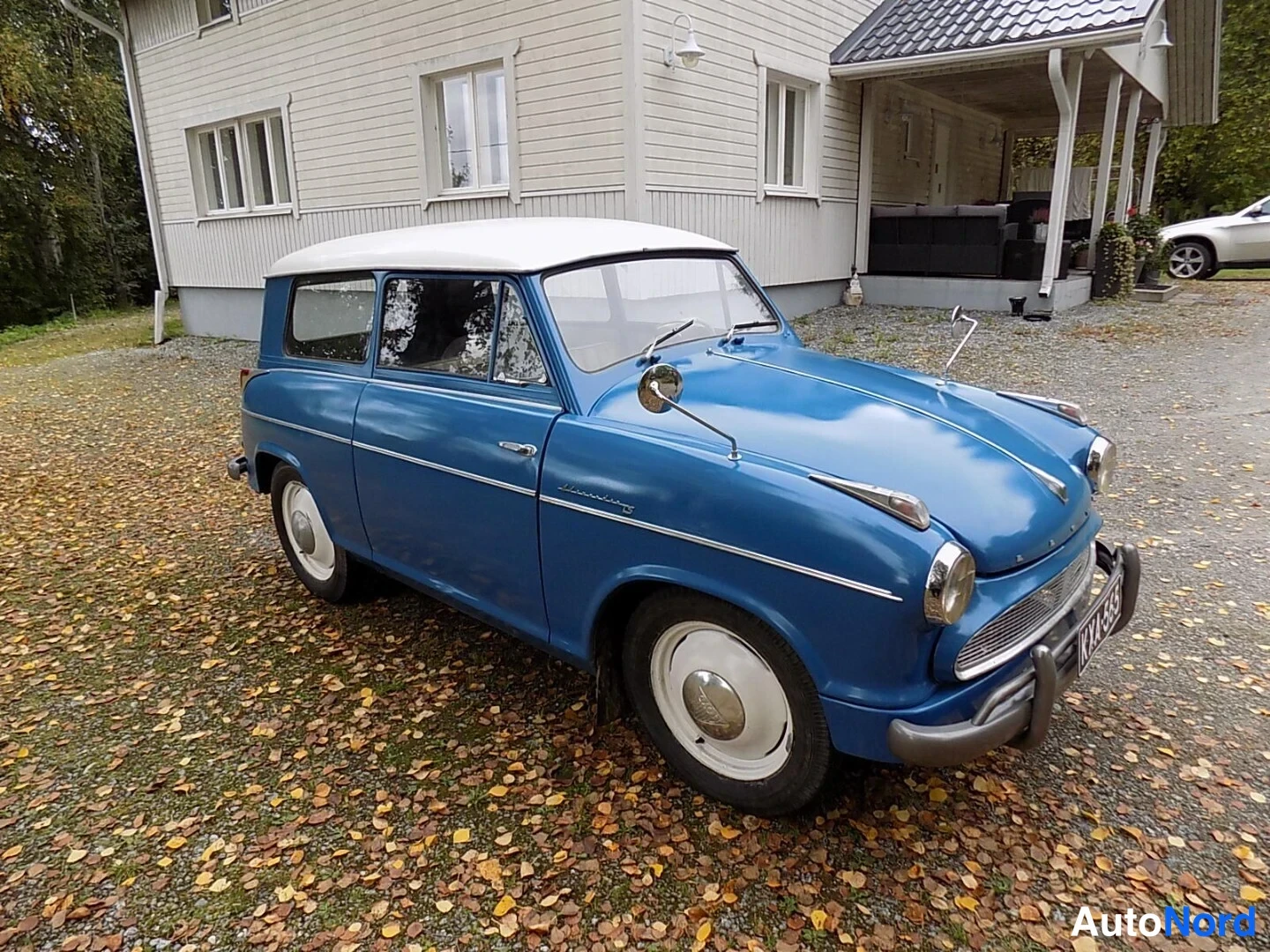 Etuviisto, nokka oikealle: Sininen vintage-auto valkoisella katolla etukulmasta talon pihalla.