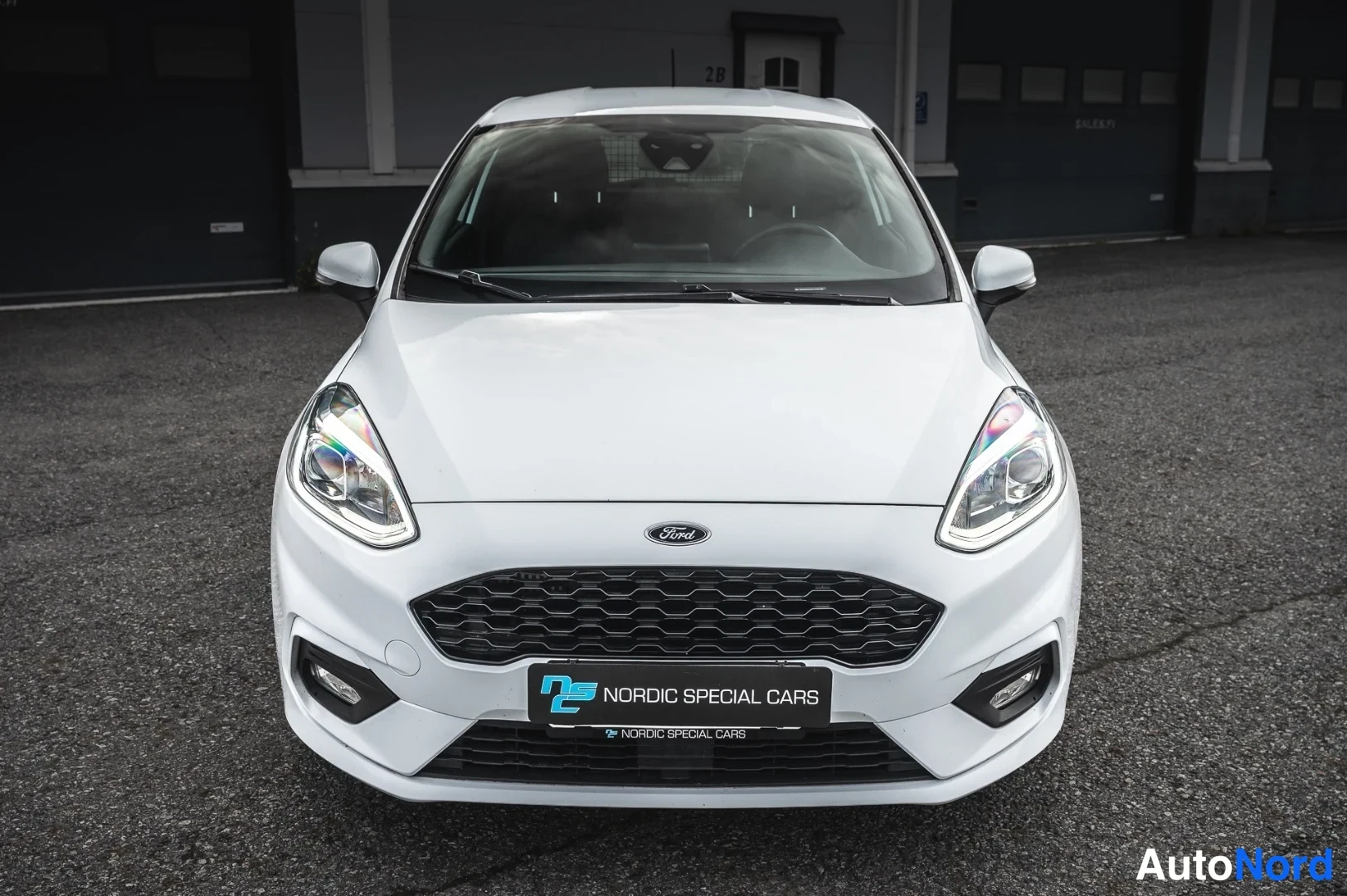 Edestä: Valkoinen Ford Fiesta suoraan edestäpäin, Ford-merkki ja musta etusäleikkö näkyvissä.