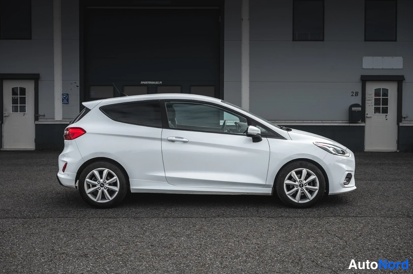 Etuviisto, nokka oikealle: Valkoinen kaksiovinen hatchback-auto sivulta kuvattuna, keula oikealla, eteinen ja perä näkyvät profiilissa.