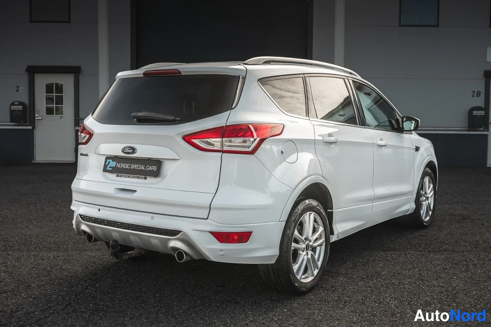 Takaviisto: Ford Kuga, valkoinen SUV takaa vasemmalta kuvattuna, perävaunukytkin näkyvissä.