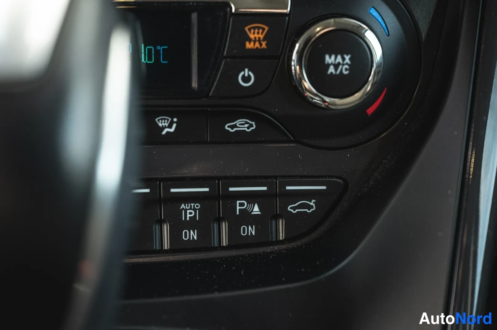 Yksityiskohta: Auton kojelaudan ilmastointilaitteen painikkeet lähikuvassa, näkyvät tekstit MAX A/C, MAX, AUTO, ON ja P ON.