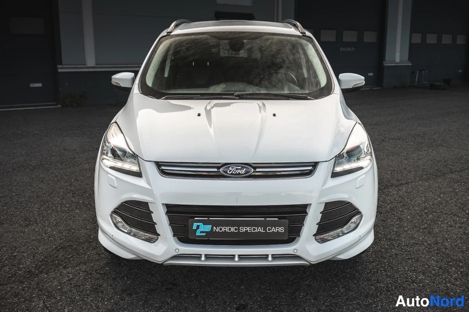 Edestä: Valkoisen Ford Kugan etunäkymä, Ford-merkki etusäleikössä ja Nordic Special Cars -kyltti etupuskurissa.