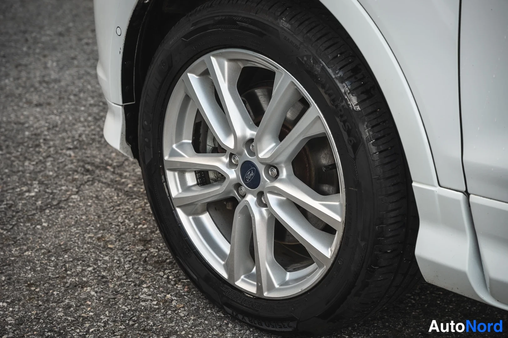 Sivulta: auton etupyörän lähikuva: hopea kevytmetallivanne, Ford-keskuskoriste, musta Goodyear-renka
