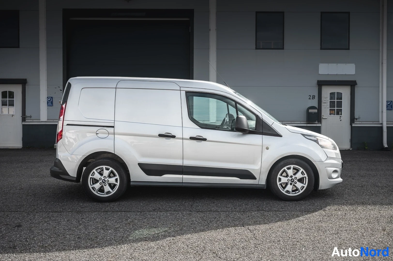 Etuviisto, nokka oikealle: Ford Transit Connect -pakettiauto sivusta hieman keulaa kohti kulmasta valokuvattuna; hopeanharmaa kori, tummat ovienkahvat ja alusroiskeet, nelipuolaise