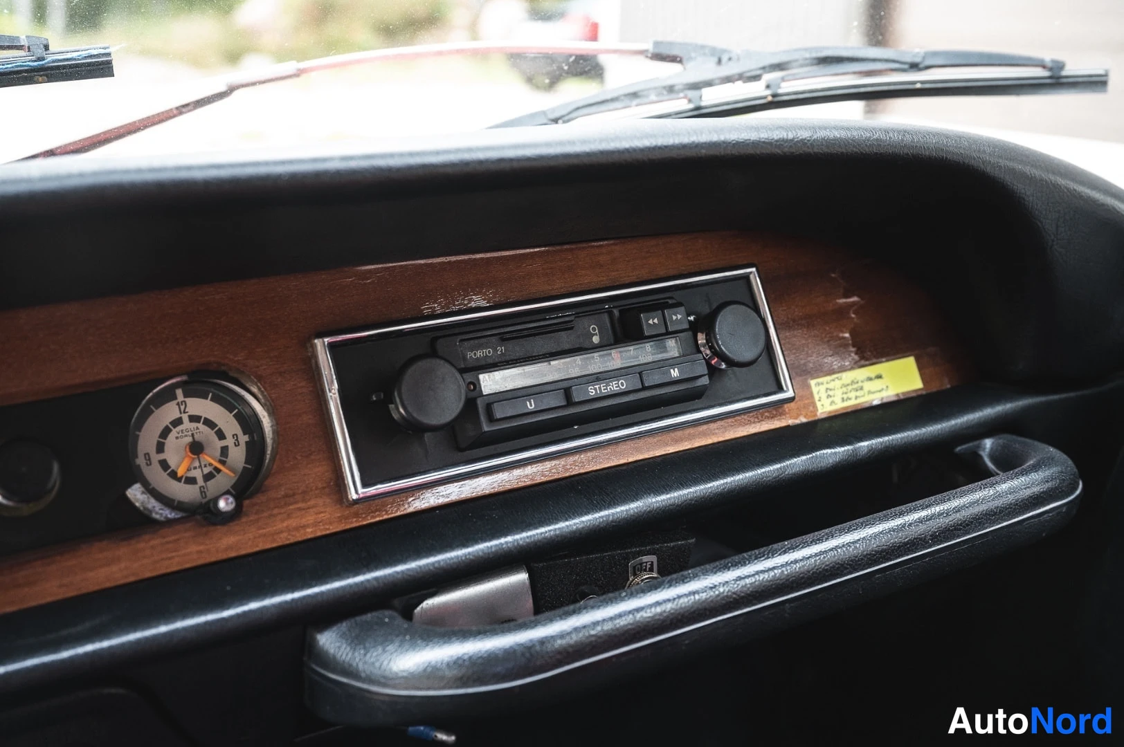 Muu: Radio ja analoginen kello kojelaudan puupanelissa; radion paneelissa lukee ”STEREO”. Keltainen muistilappu paneelin oikealla puolella.
