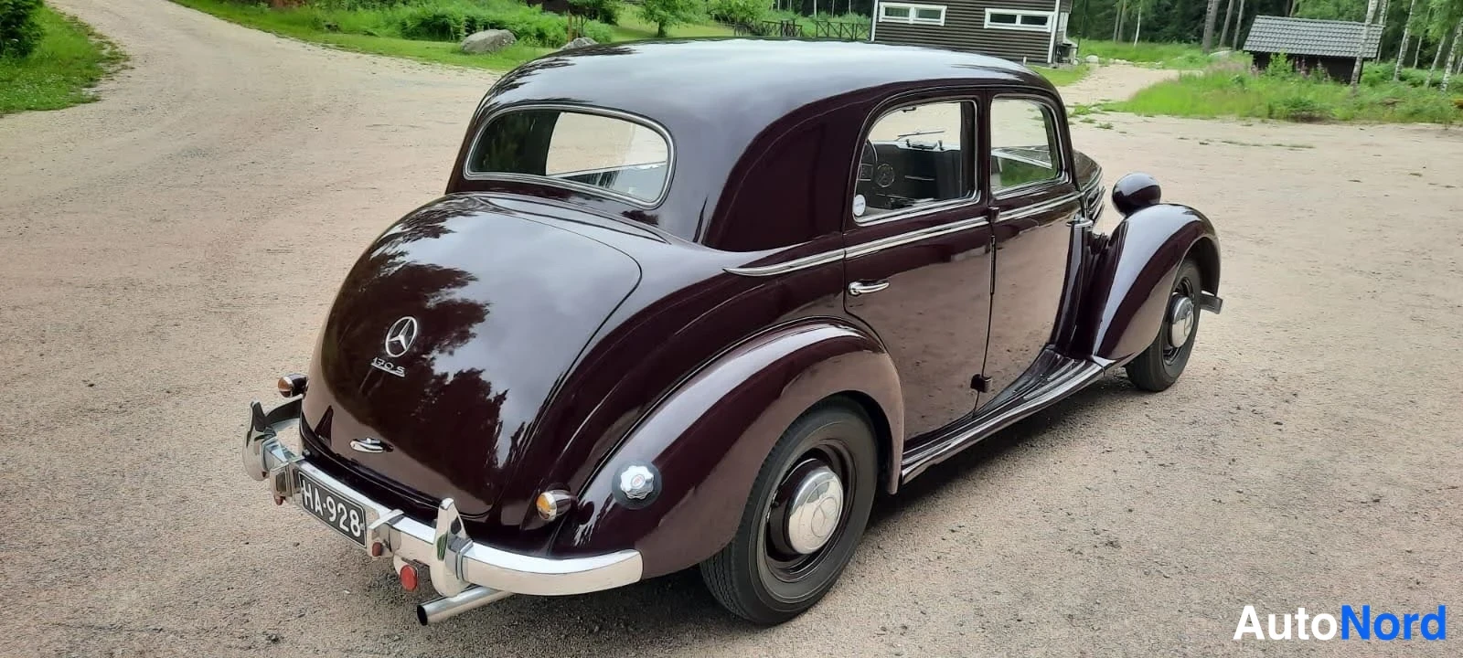 Takaviisto: Tummanpunainen Mercedes-Benz Sb -sihtiauto takaviistokuvassa hiekkapihalla.