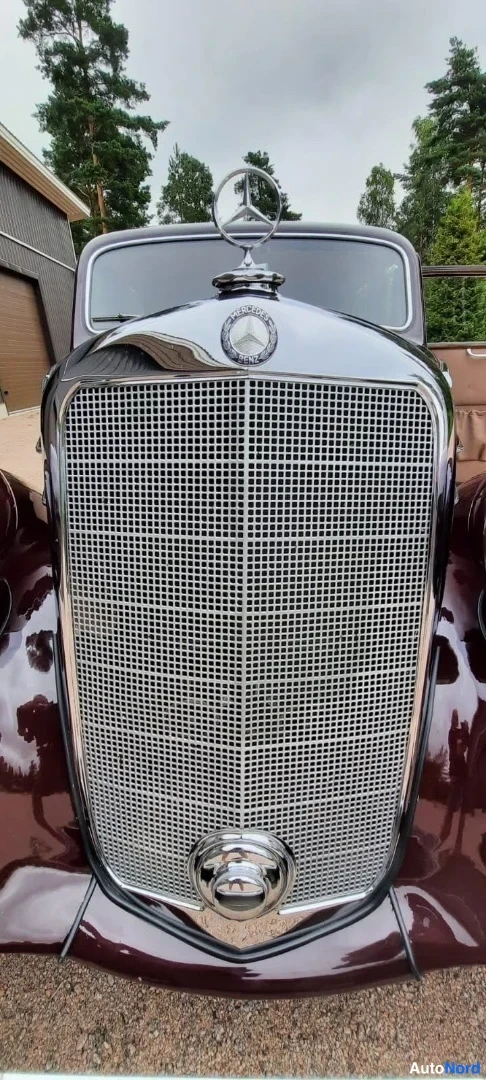 Edestä: Mercedes-tähtikoriste ja kromattu jäähdytinkeitko suoraan edestä kuvattuna; konekansi tummanpunaisena.