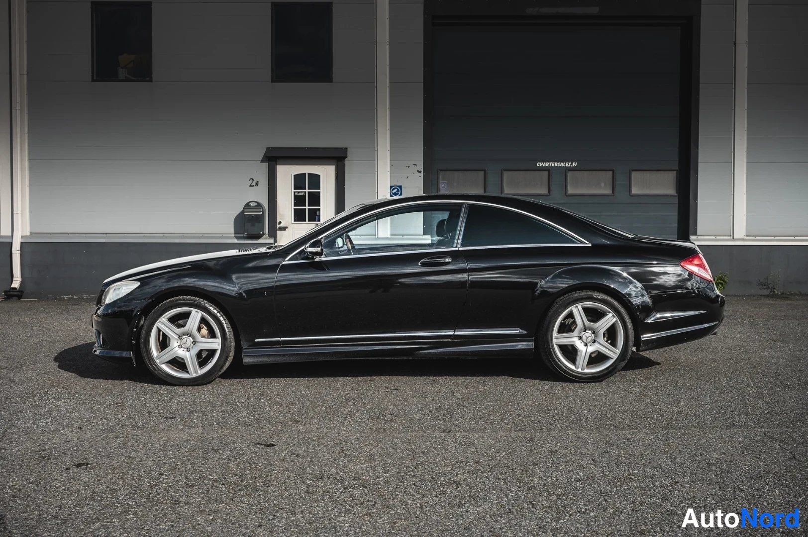 Sivulta: Mustan coupé-auton sivuprofiili kadulla rakennuksen edessä.