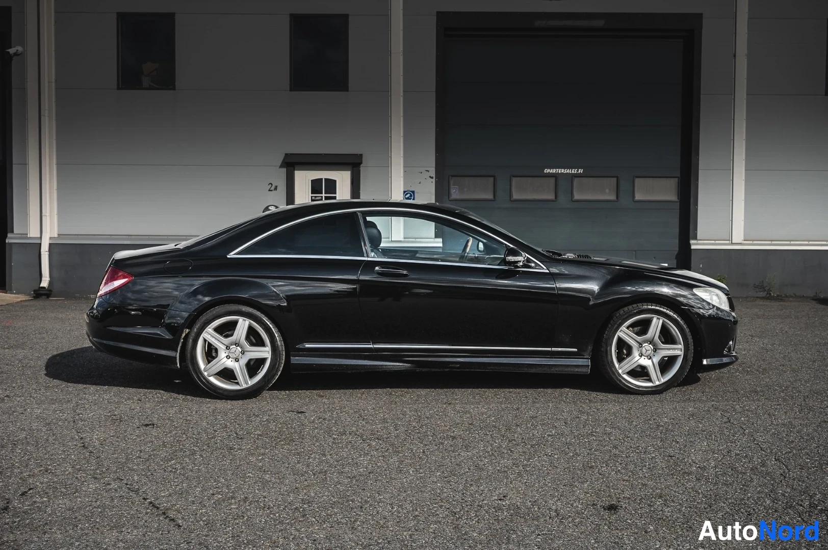 Sivulta: Mustan Mercedes-Benz CL 550:n sivuprofiili; pitkä kaksiovinen kori, kromilista ja viisisakaraiset kevytmetallivanteet erottuvat auton ollessa paikoillaan asfalt