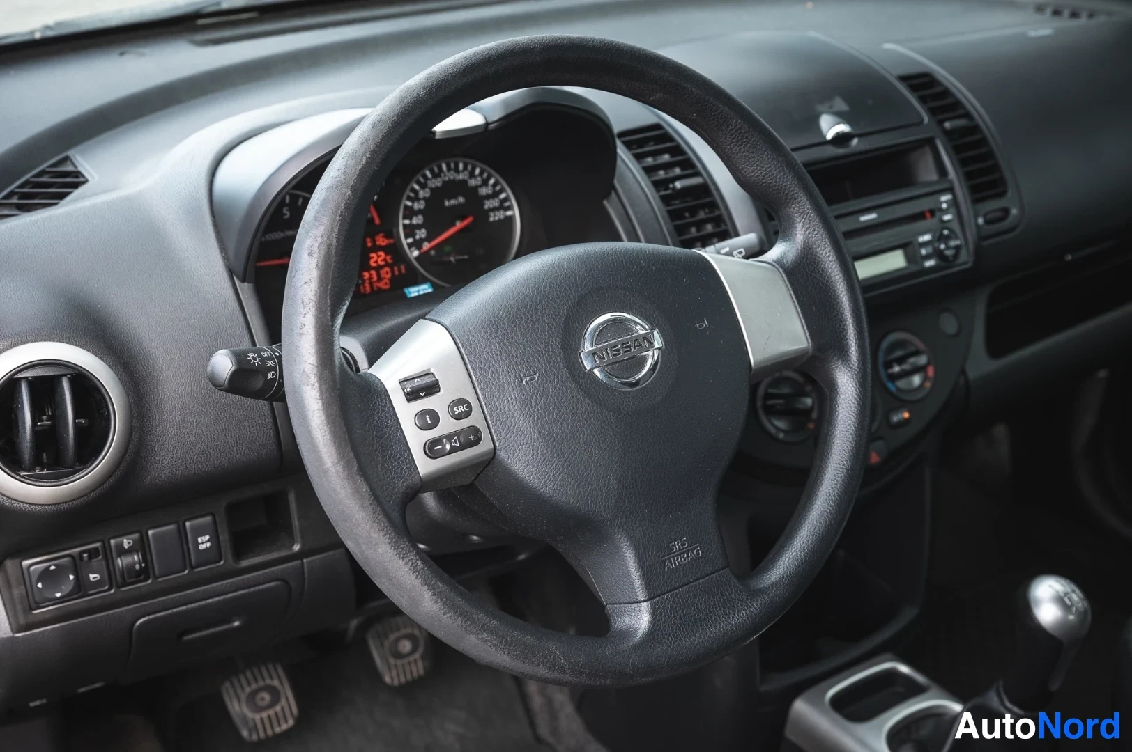 Muu: Ohjaamon lähikuva: Nissan-ohjauspyörä, mittaristo ja radio keskikonsolissa.