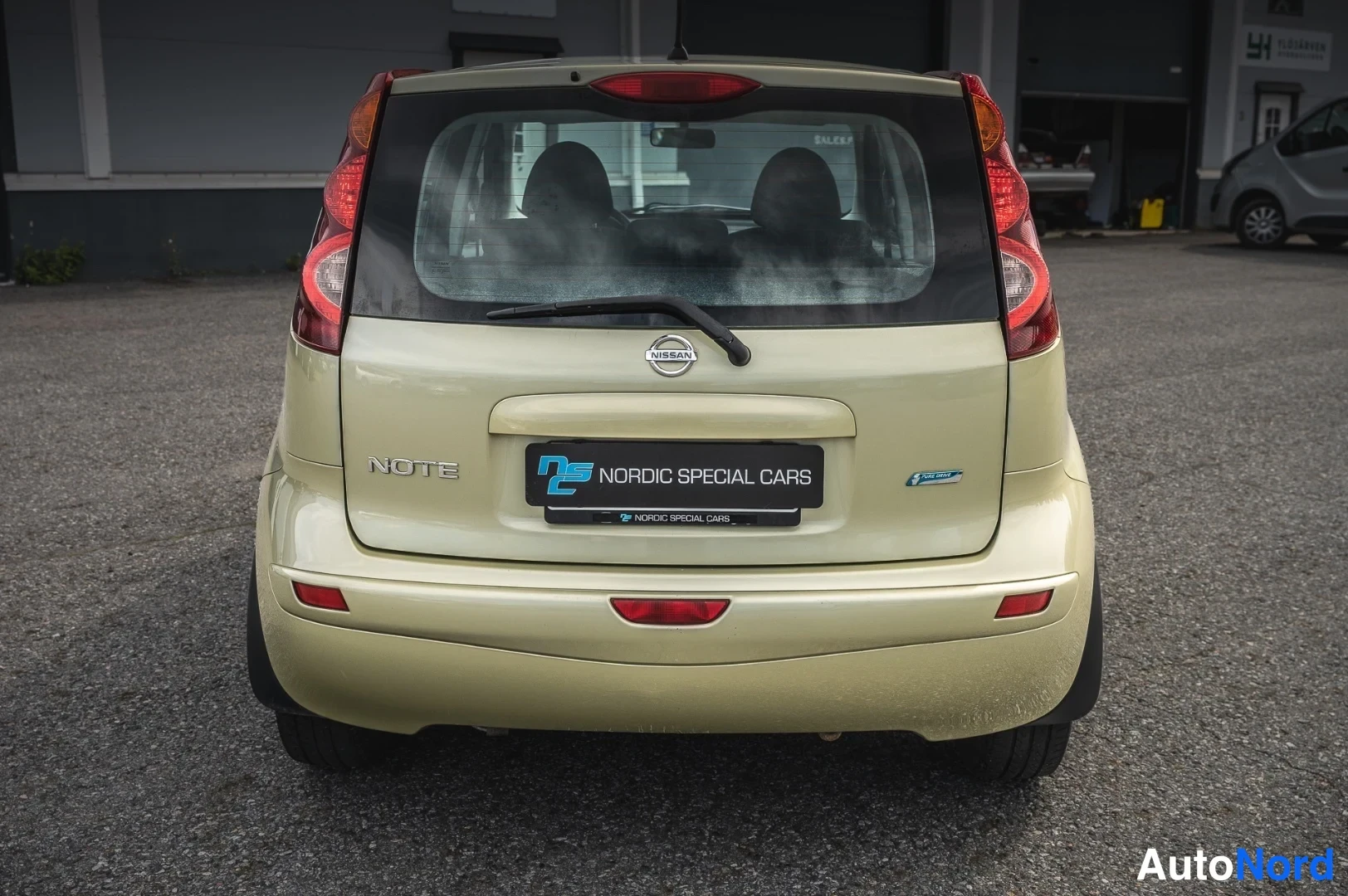 Takaa: Nissan Note -auto kuvattuna suoraan takaa; näkyvissä takavalot, Nissan-merkki, NOTE-kirjoitus, takanäytin ja Nordic Special Cars -kilpi.