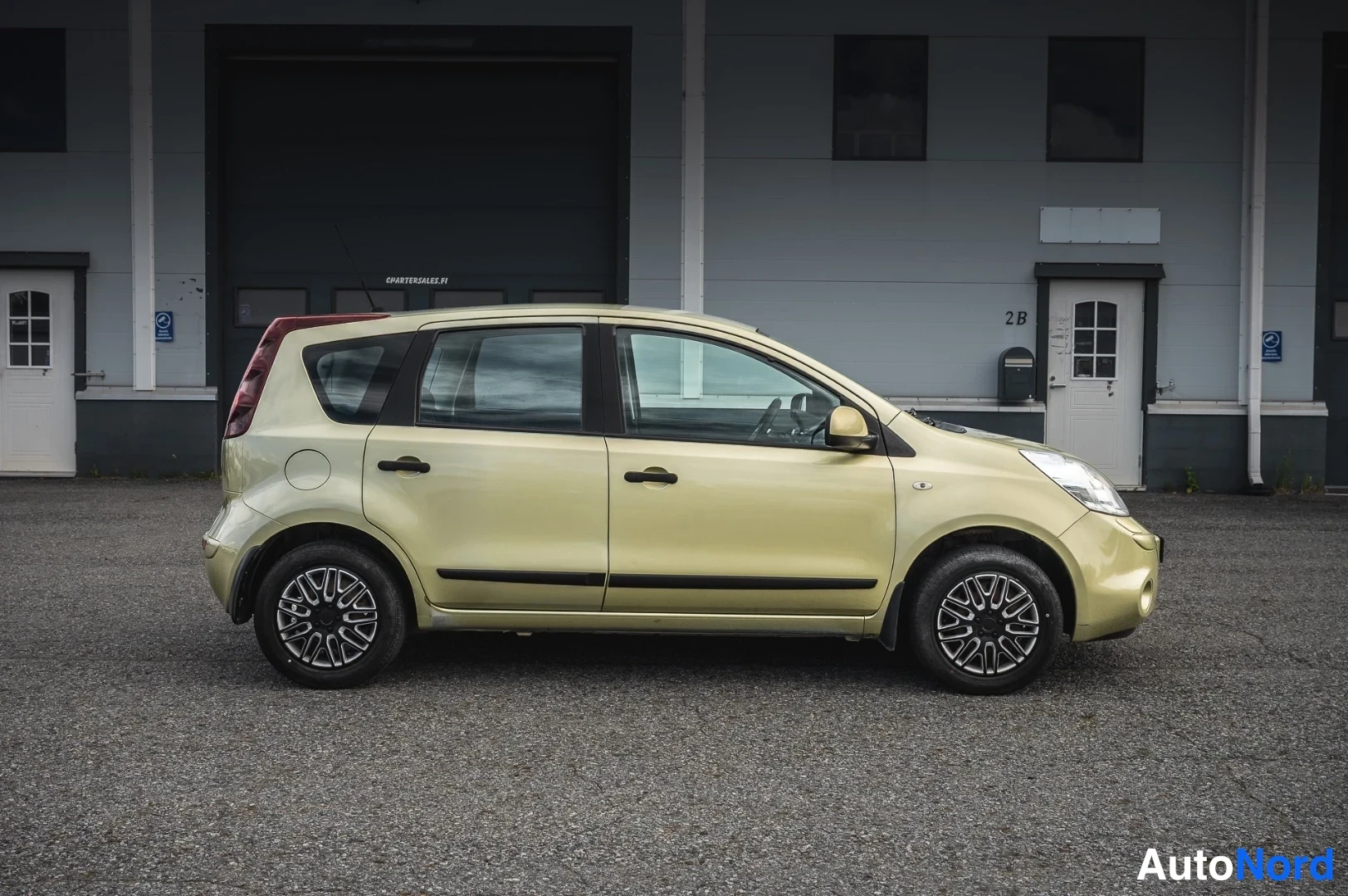 Sivulta: Nissan Note sivuprofiilikuvassa: vaalean kellertävä kori, neljä ovea, mustat ovenkahvat ja rei'itetyt kevytmetallivanteet.