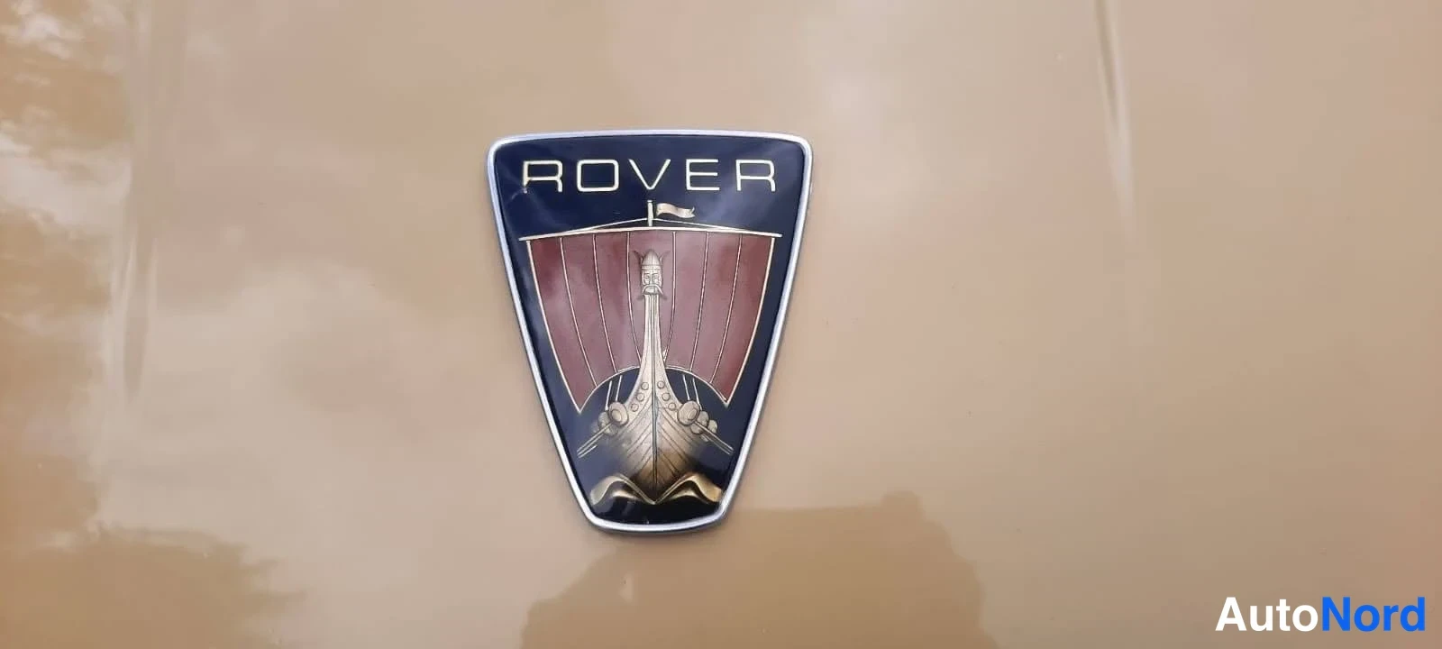 Yksityiskohta: Rover-merkki vaaleanruskealla konepeltipinnalla.