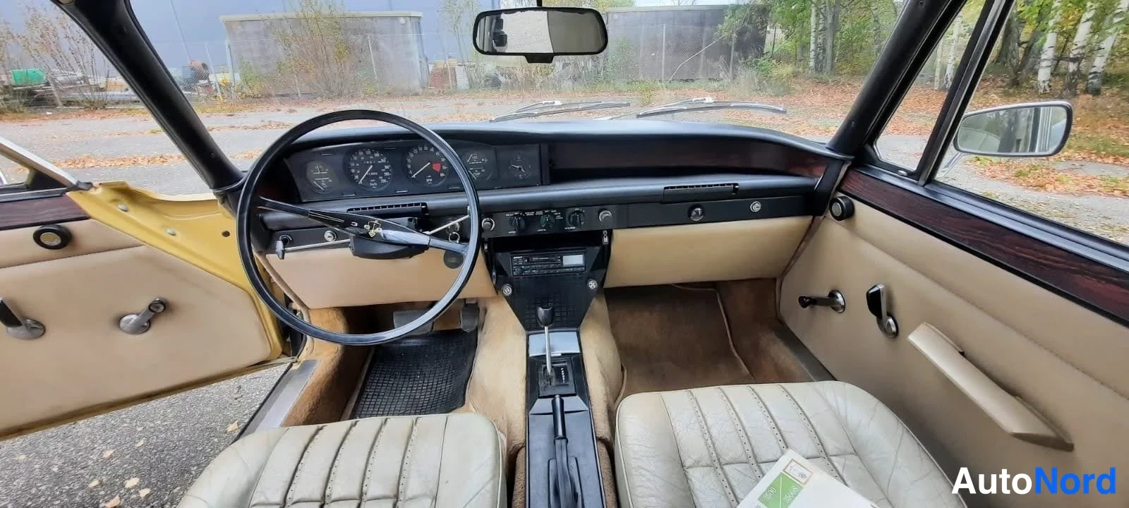 Muu: Auton sisätilat: beige verhoilu ja paneelit, ohjauspyörä oikealla, automaattivaihteen keila keskitunnelissa, mittaristo ja klassinen kojelauta.
