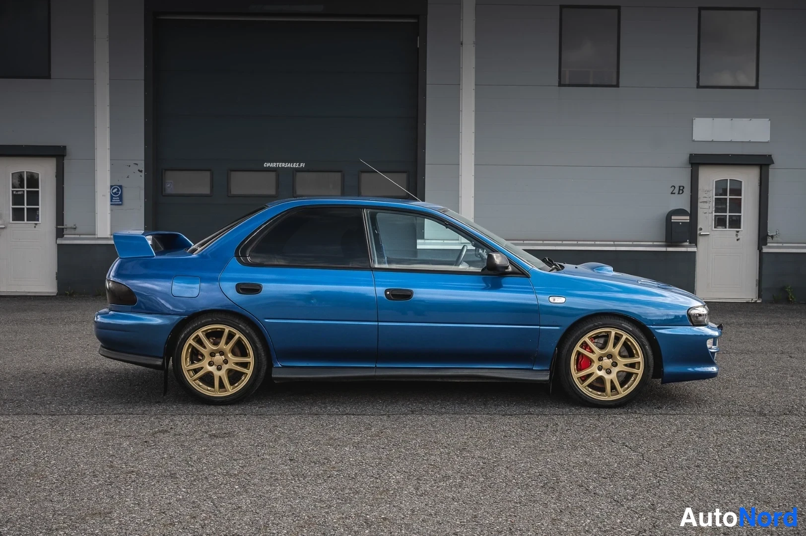 Sivulta: Sininen Subaru Impreza sivulta kuvattuna, kultavanteiset pyörät ja punaiset jarrusatulat.