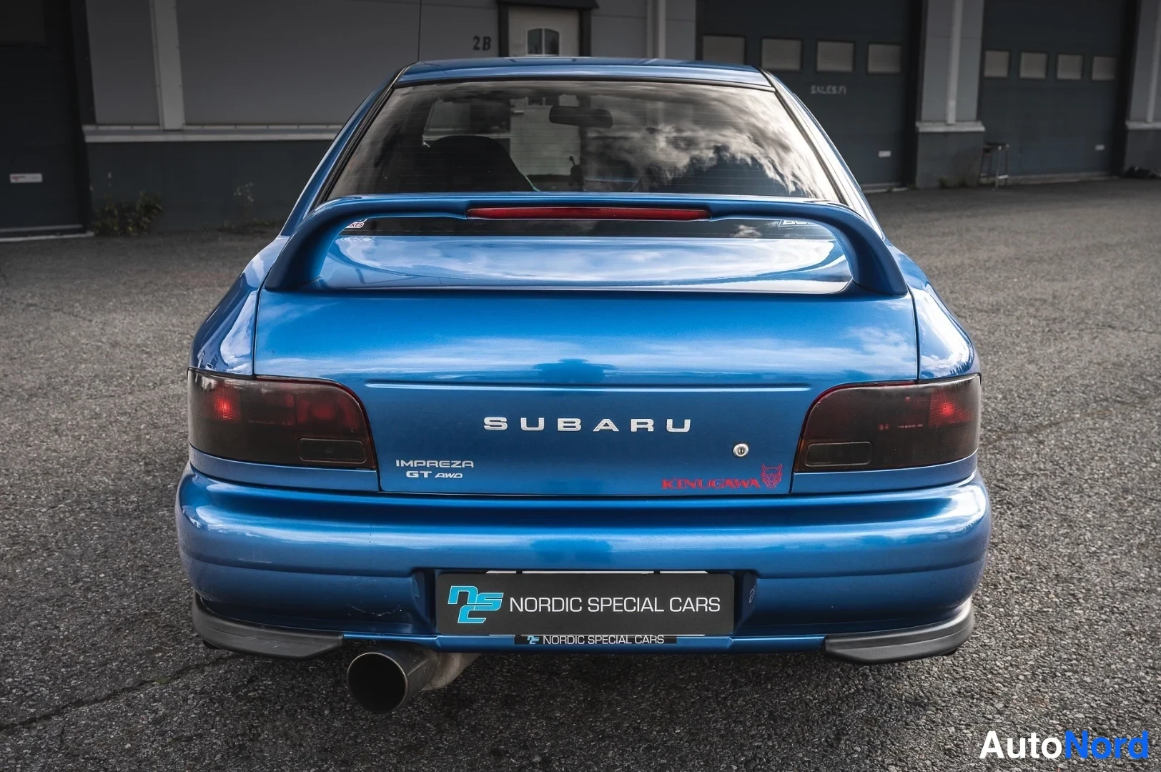 Takaa: Kuva 1: Sininen Subaru Impreza takaa kuvattuna, suuri takasiipi ja kaksiosainen pakoputki.