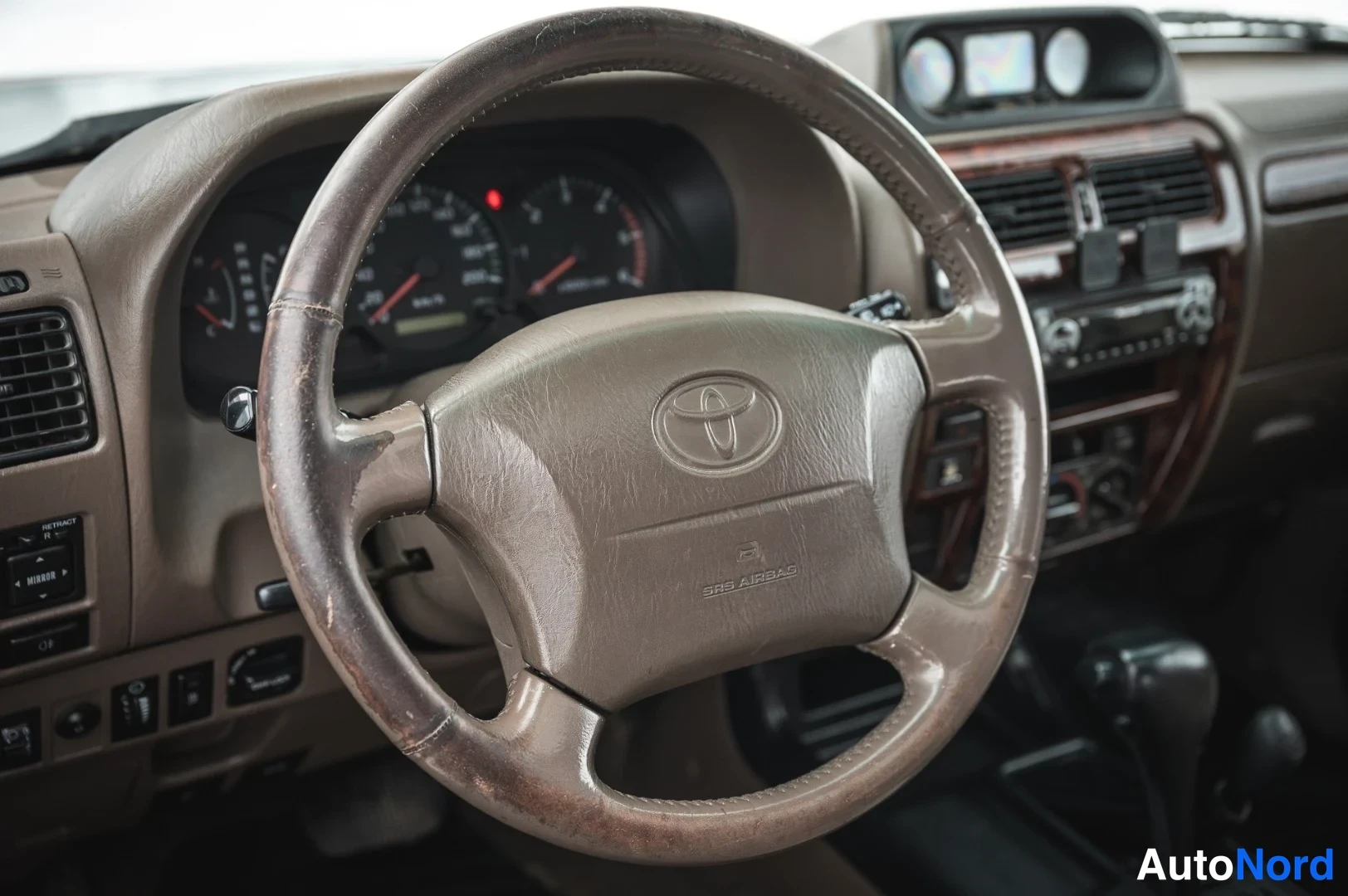 Edestä: Ohjaamossa ruskea Toyota-ohjauspyörä, jossa SRS AIRBAG -teksti, kojelauta ja varusteita taustalla.