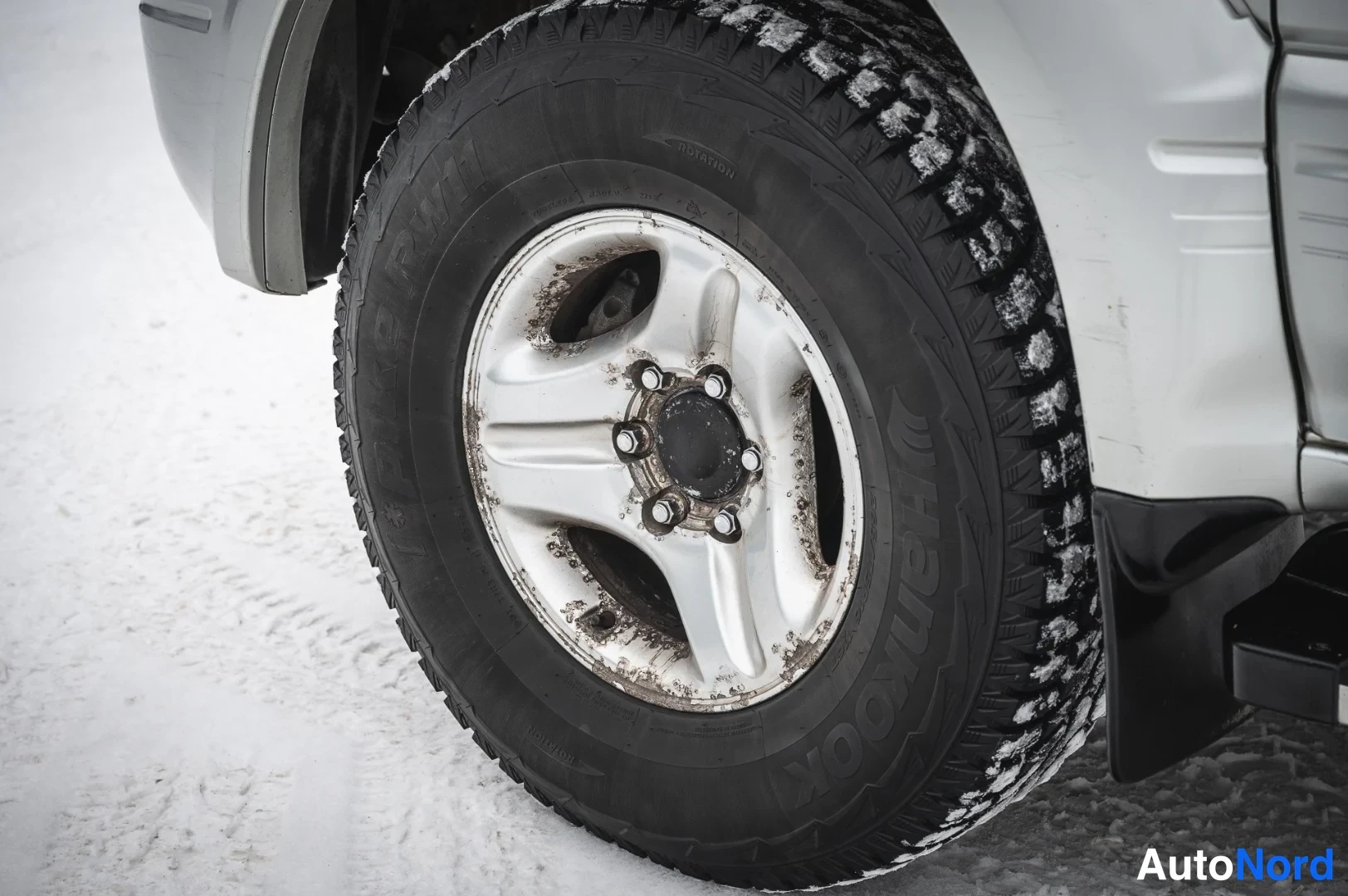 Yksityiskohta: Sama pyörän lähikuva toistettuna: Hankook-talvirengas lumessa kevytmetallivannessa.