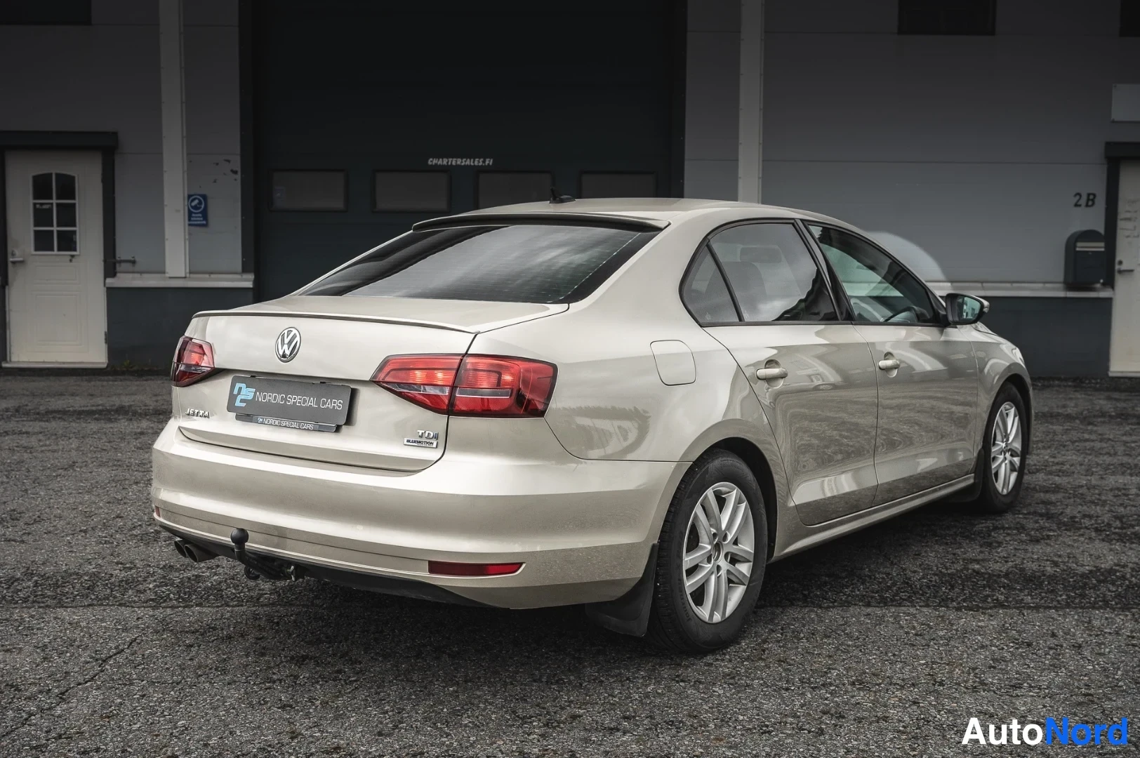 Takaviisto: Volkswagen Jetta -sedanin takaosa ja sivuprofiili kolmannelta neljäsosalta, vaaleanbeige runko, takavalot ja perävaunukoukku näkyvissä.