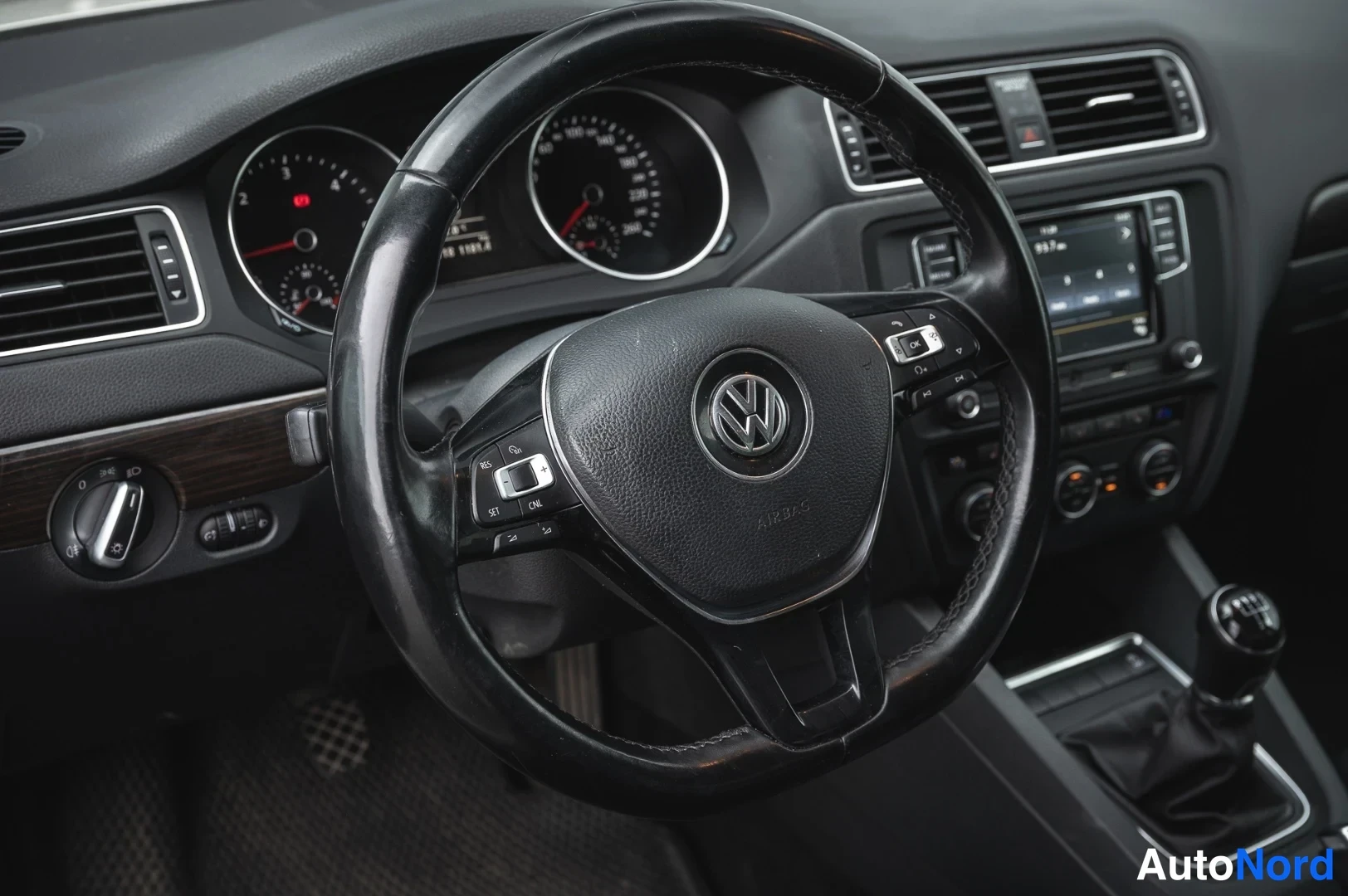 Muu: VW-merkkinen monitoimiohjauspyörä ja mittaristo lähikuvassa; radio ja manuaalivaihteen keppi näkyvät osittain.