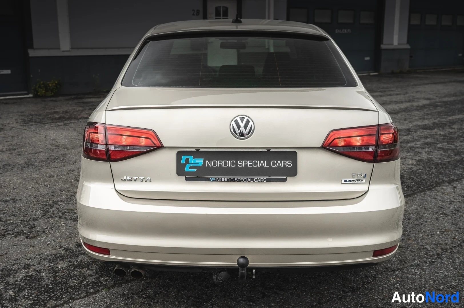 Takaa: Volkswagen Jetta takaa nähtynä, beige värillä, trailerikoukku ja kaksoispakoputki näkyvissä.