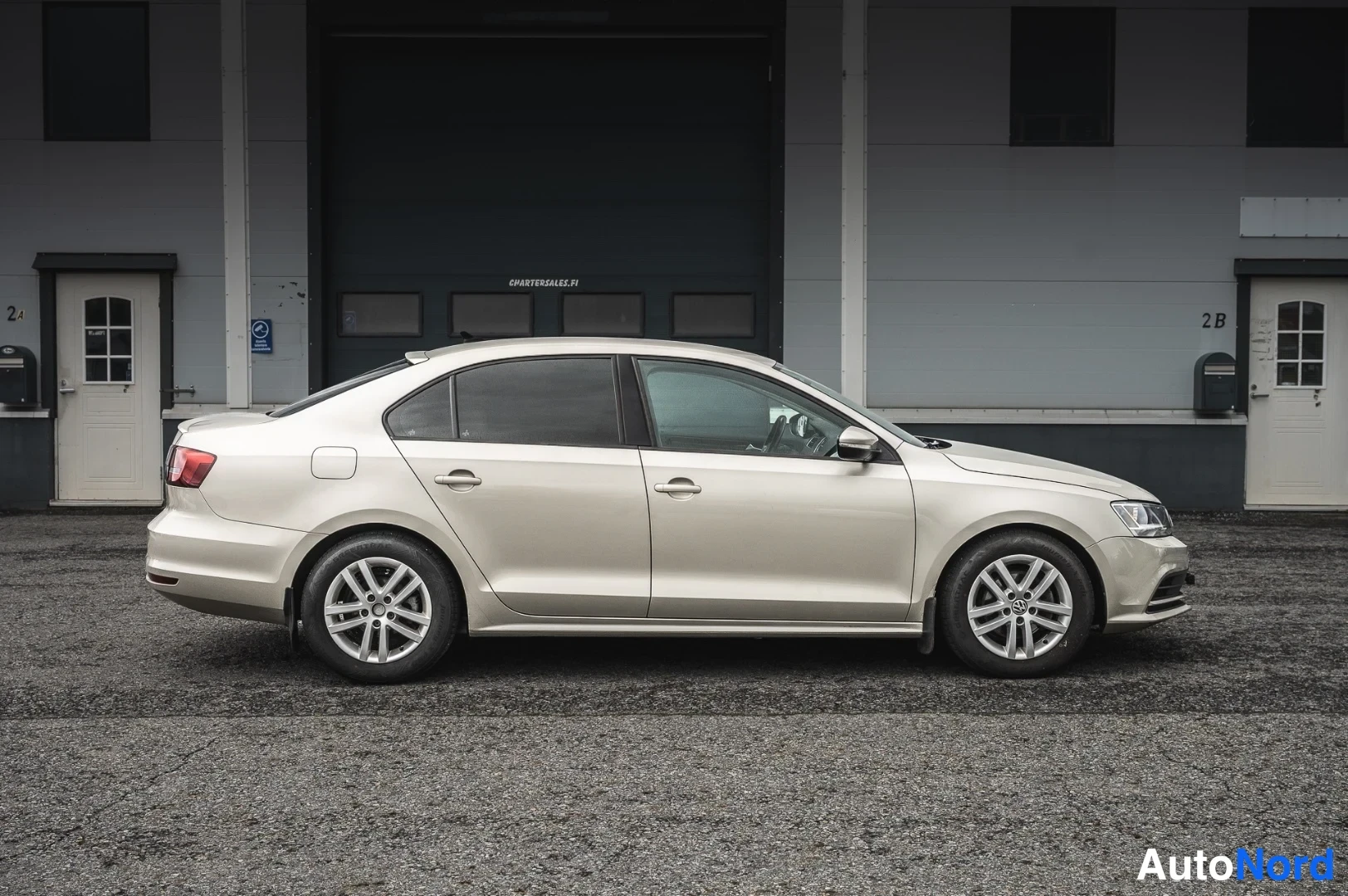 Etuviisto, nokka oikealle: Volkswagen Jetta -sedanin etukulma oikealta, vaaleanbeige runko, Hopeispro-namekombi.