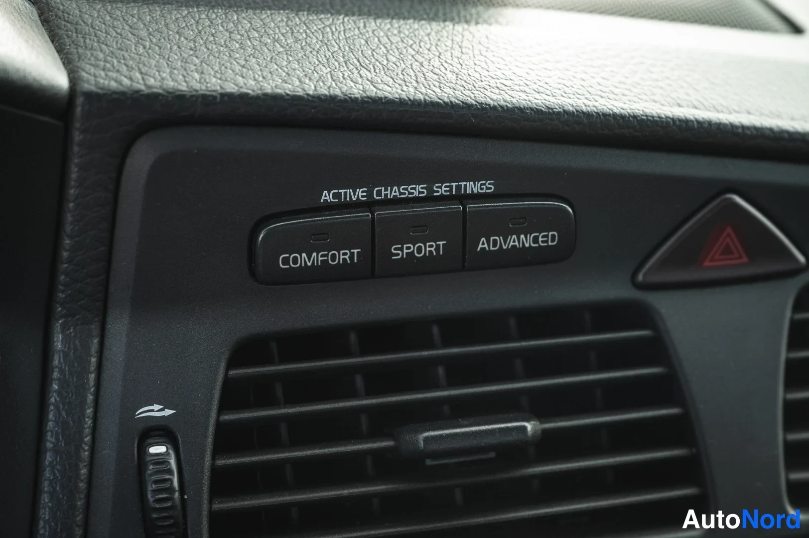 Muu: Kojelaudan nappiryhmä ACTIVE CHASSIS SETTINGS, painikkeet COMFORT, SPORT ja ADVANCED, vieressä varoitusvilkkunappi.
