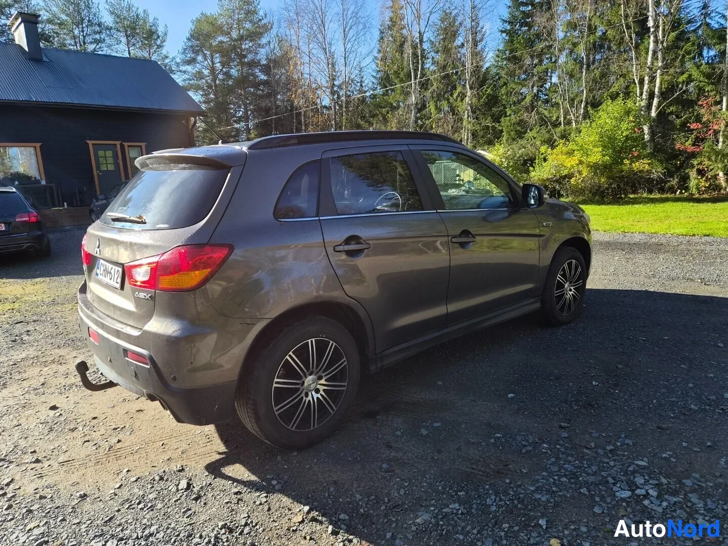 Takaviisto: Korkealta otettu rear three_quarter kuva ruskean harmaan Mitsubishi ASX -autosta, jossa näkyy takapää ja oikea sivu. Takavalot ovat kirkkaan punaiset ja takapus