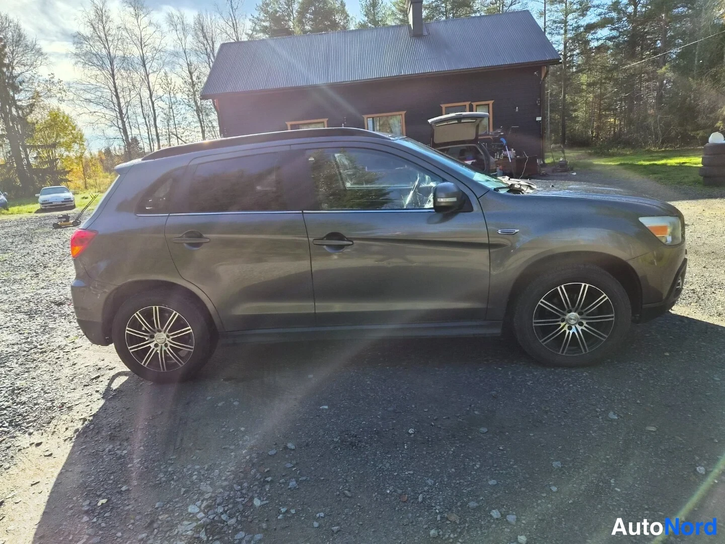 Takaviisto: Tummanharmaa Mitsubishi ASX -maasturin kylki ja takakulma sorapihalla, takavalo ja kolme pyörää näkyvissä.