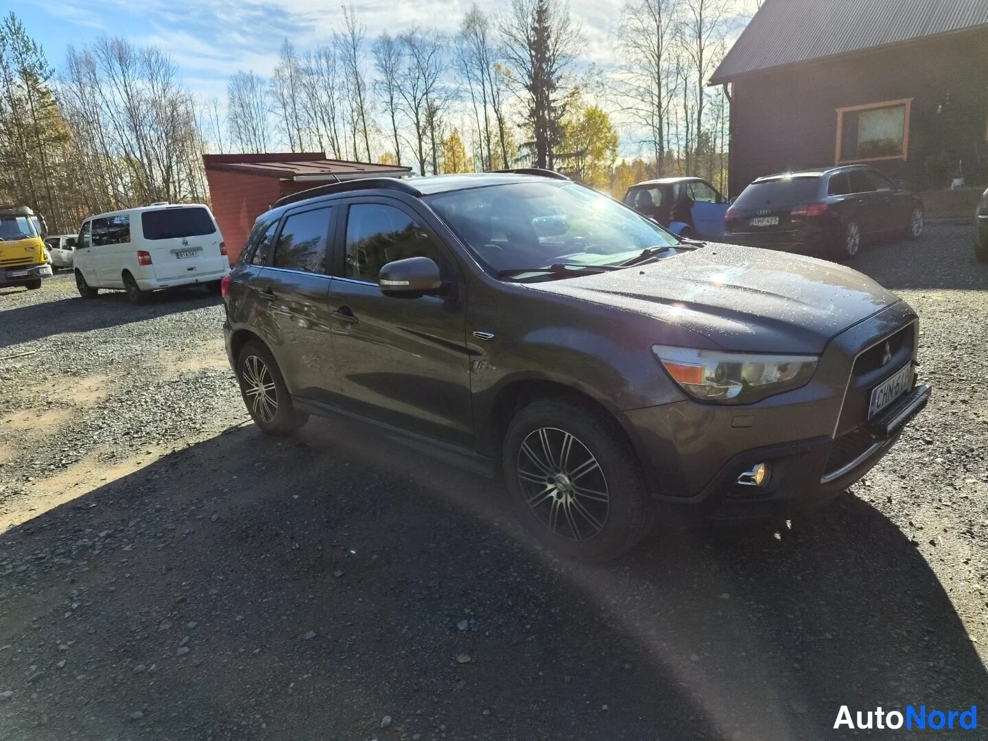Etuviisto, nokka oikealle: Tummanharmaa Mitsubishi ASX etu-vinoukulmasta keula oikealla soraparkissa, muut ajoneuvot taustalla.