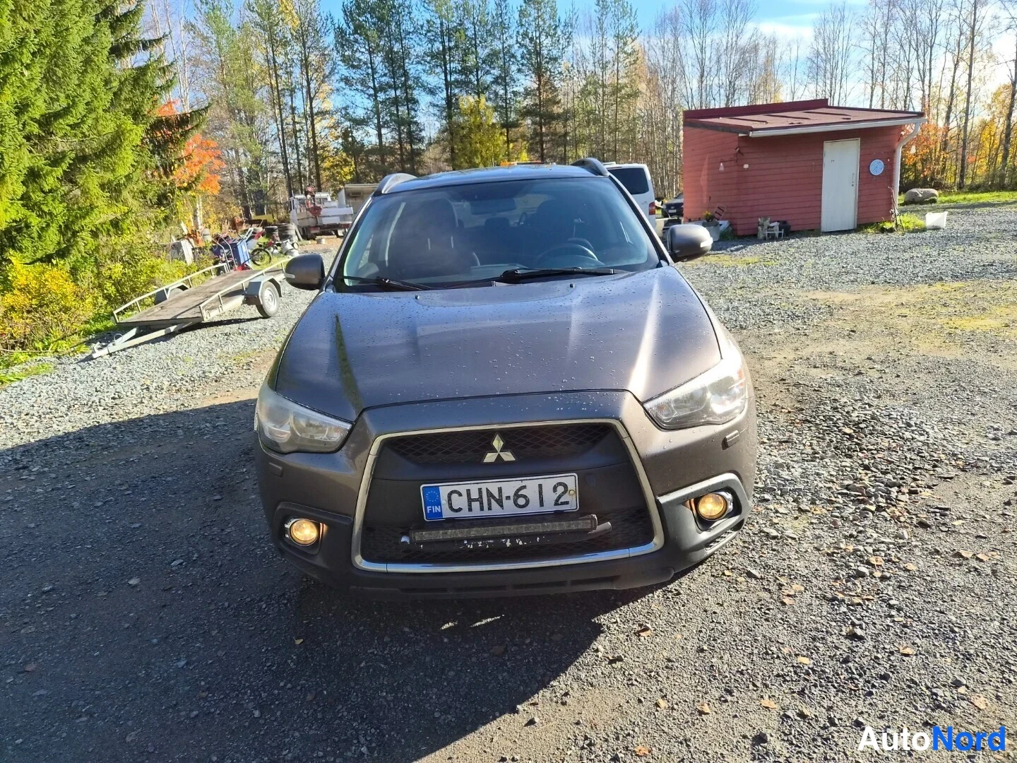 Edestä: Mitsubishi ASX -henkilöauto edestä kuvattuna sorapintaan pysäköituna, rekisteritunnus, kori ruskeanharmaa.