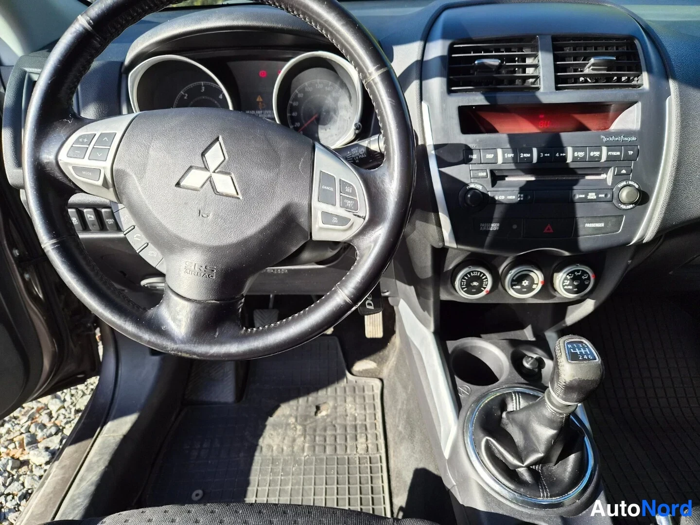 Edestä: Ohjaamo suoraan edestä kuvattuna: Mitsubishi-ohjauspyörä, mittaristo, radio ja kolme säätönuppia, manuaalivaihtaja.