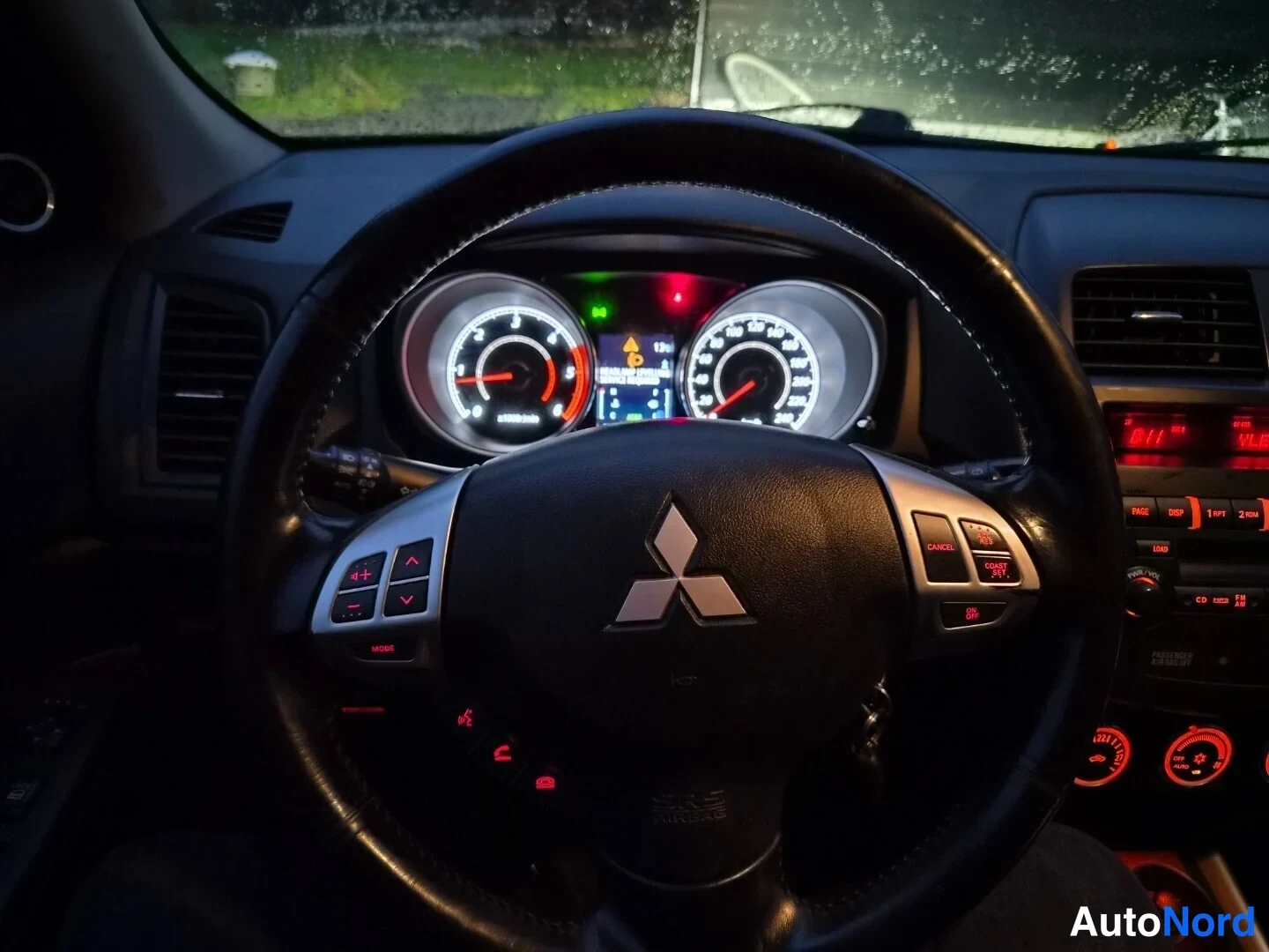 Yksityiskohta: Ohjaamokuva Mitsubishi-ohjauspyörästä ja kojelaudan mittareista pimeässä.