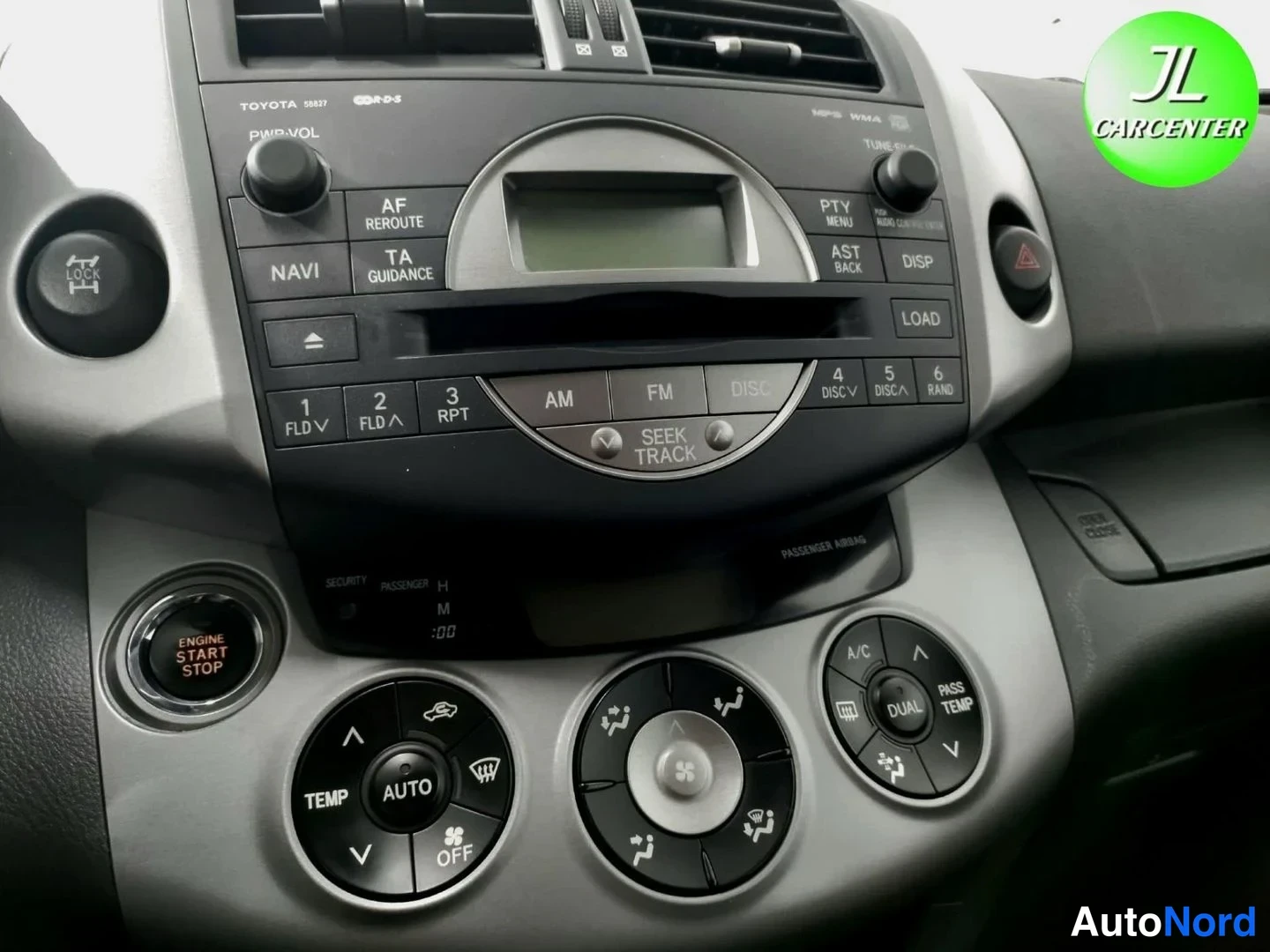 Yksityiskohta: Kojelaudan keskikonsoli: radio-CD-yksikkö näytöllä ja monilla painikkeilla, alla automaattinen ilmastointipaneeli (TEMP/AUTO/DUAL) ja ENGINE START STOP -käynnis