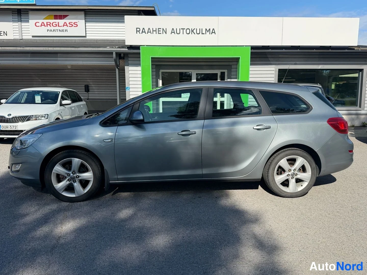 Sivulta: Opel Astra -farmari sivulta kuvattuna autokoripihan edessä, taustalla Carglass- ja Raahen Autokulma -kyltit.