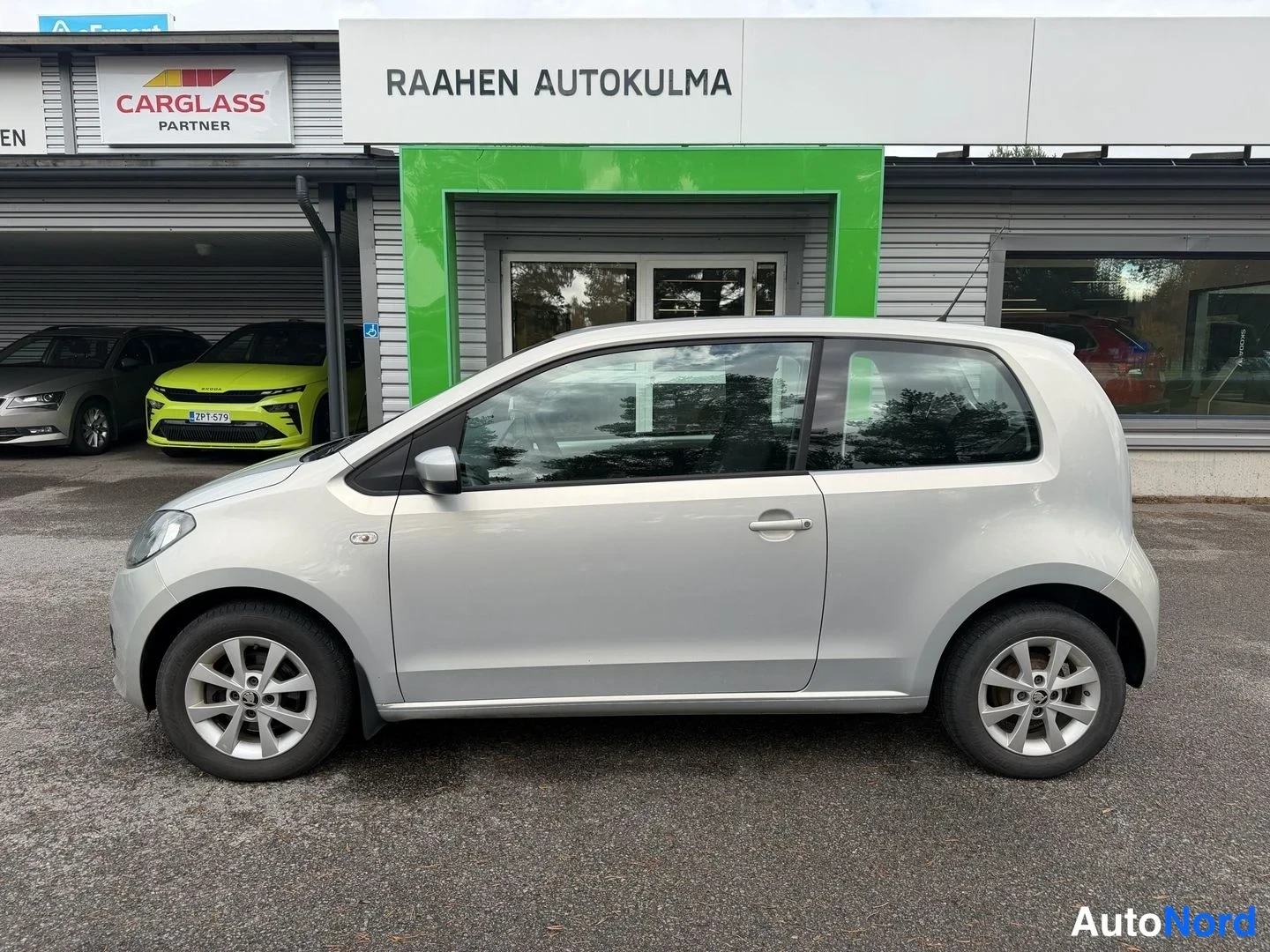 Sivulta: Hopeinen kaksiovinen Skoda Citigo sivukuvassa autoliikkeen seinustalla.