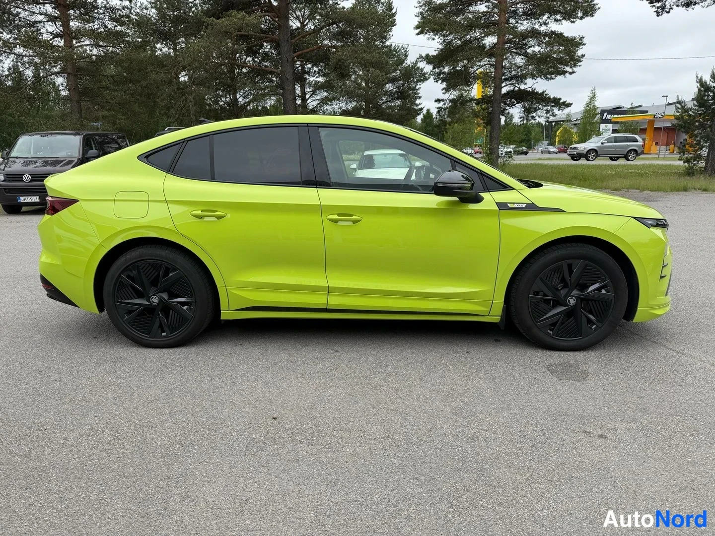 Sivulta: Kirkkaanvihreän coupé-SUV:n sivukuva; mustat viistaevät ja mustat kevytmetallivanteet näkyvät parkkipaikalla puiden edustalla.