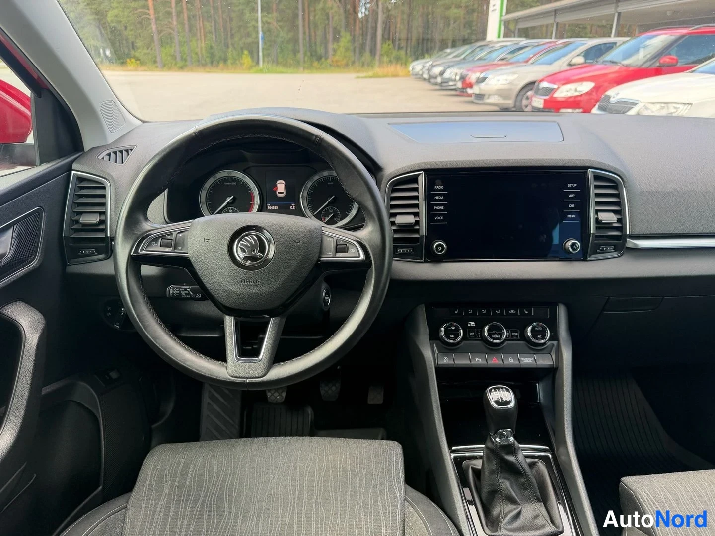 Yksityiskohta: Skoda-ohjauspyörä, analogiset mittarit, keskellä kosketusnäyttö ja manuaalivaihteen keppi, tumma sisusta.