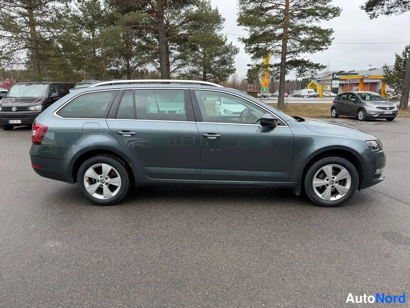 Sivulta: Harmaa farmariauto sivulta kuvattuna parkkipaikalla, katto-spoilerit ja hopeiset vanteet näkyvät.