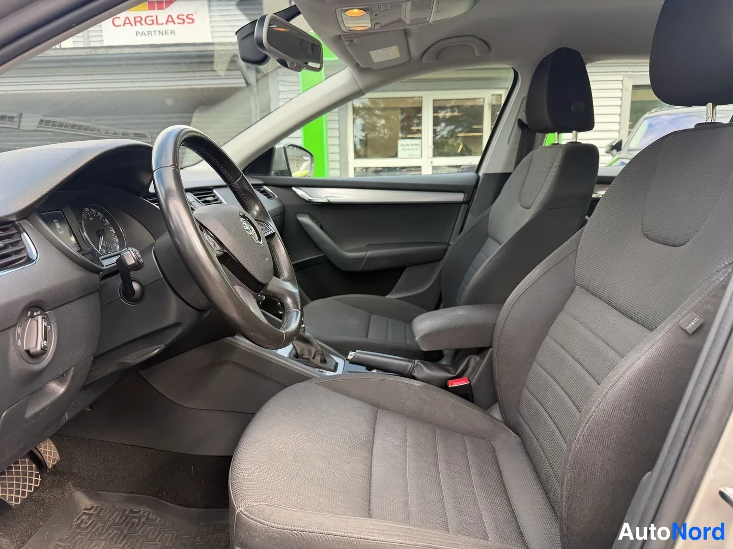 Muu: Autojen sisätilat: etupenkit ja ohjaamo mustilla kankailla, Carglass-kyltti taustalla ikkunan takana.