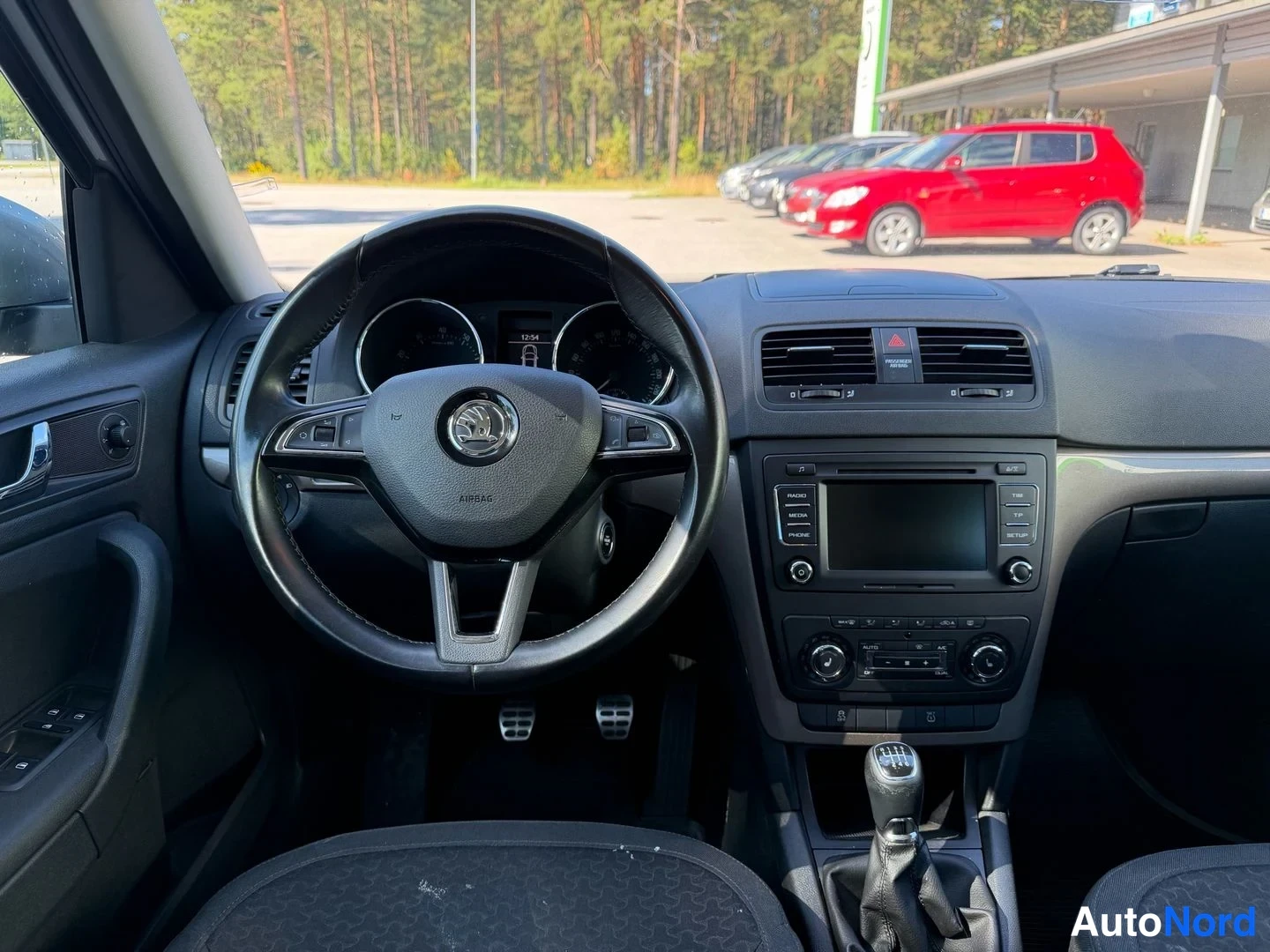 Muu: Ohjaamo etukädestä: Skoda-ohjauspyörä, mittaristo, keskikonsolissa kosketusnäyttöinen radio ja manuaalivaihteen keila.