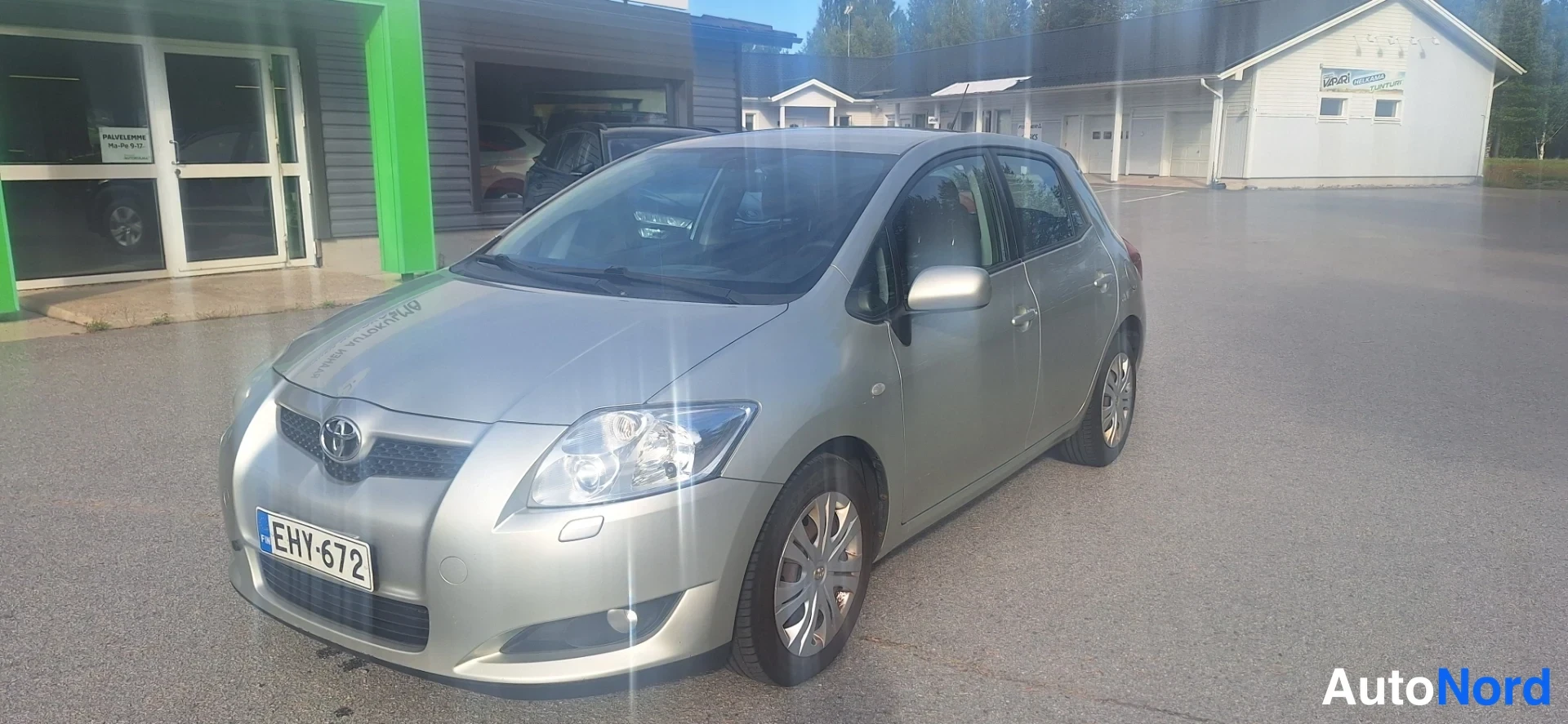 Etuviisto, nokka vasemmalle: Hopeanvärinen Toyota Auris -henkilöauto edestä vasemmasta kulmasta, rekisterikilpi.